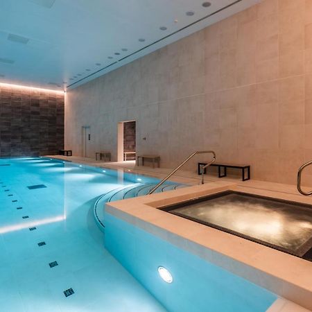 Citysuites 2 Aparthotel Manchester Exterior photo The photo shows an indoor swimming pool area. The pool is a bright blue color and features smooth, tiled surfaces. On one side, there is a hot tub area with steps leading into it. The walls are made of light-colored stone, and there is ambient lighti