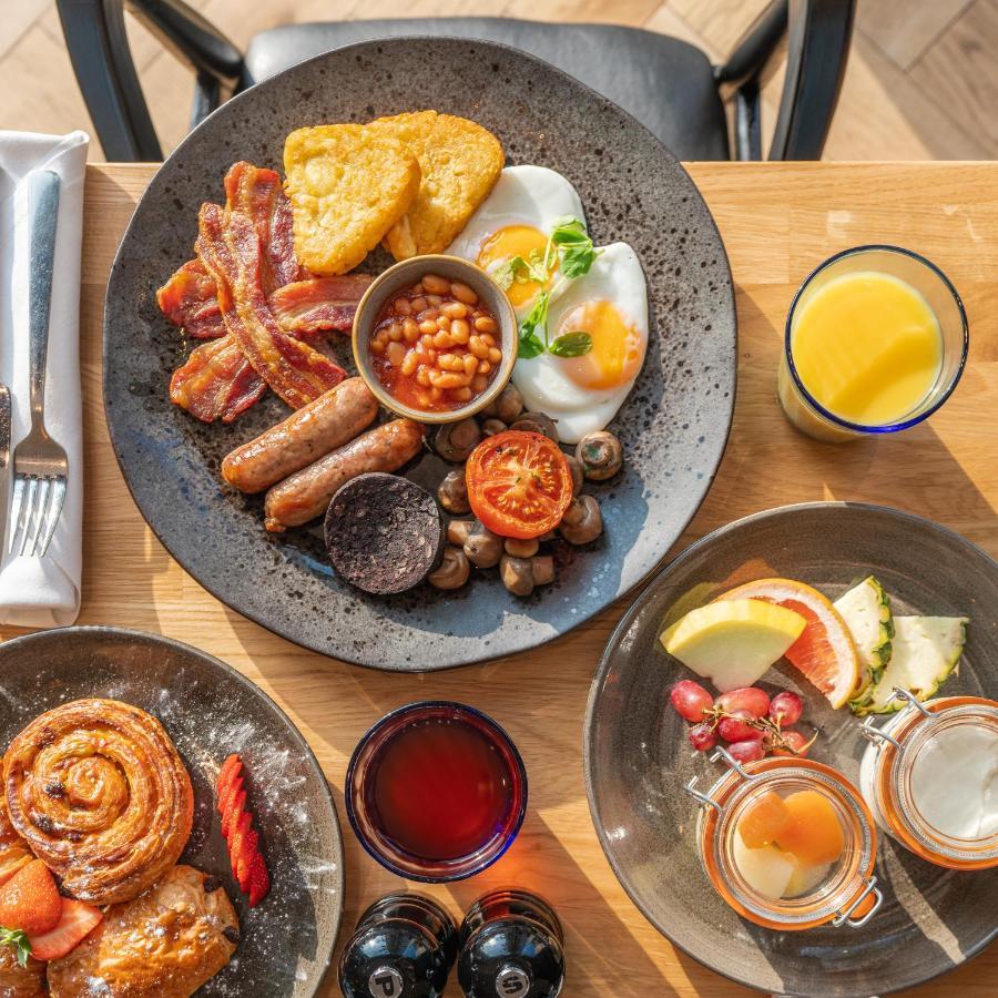 Citysuites 2 Aparthotel Manchester Exterior photo The photo showcases a delicious breakfast spread. On a large, dark plate, there are items including crispy bacon, two fried eggs, baked beans, a grilled tomato, sautéed mushrooms, sausage links, and slices of black pudding. There's also a few pieces 