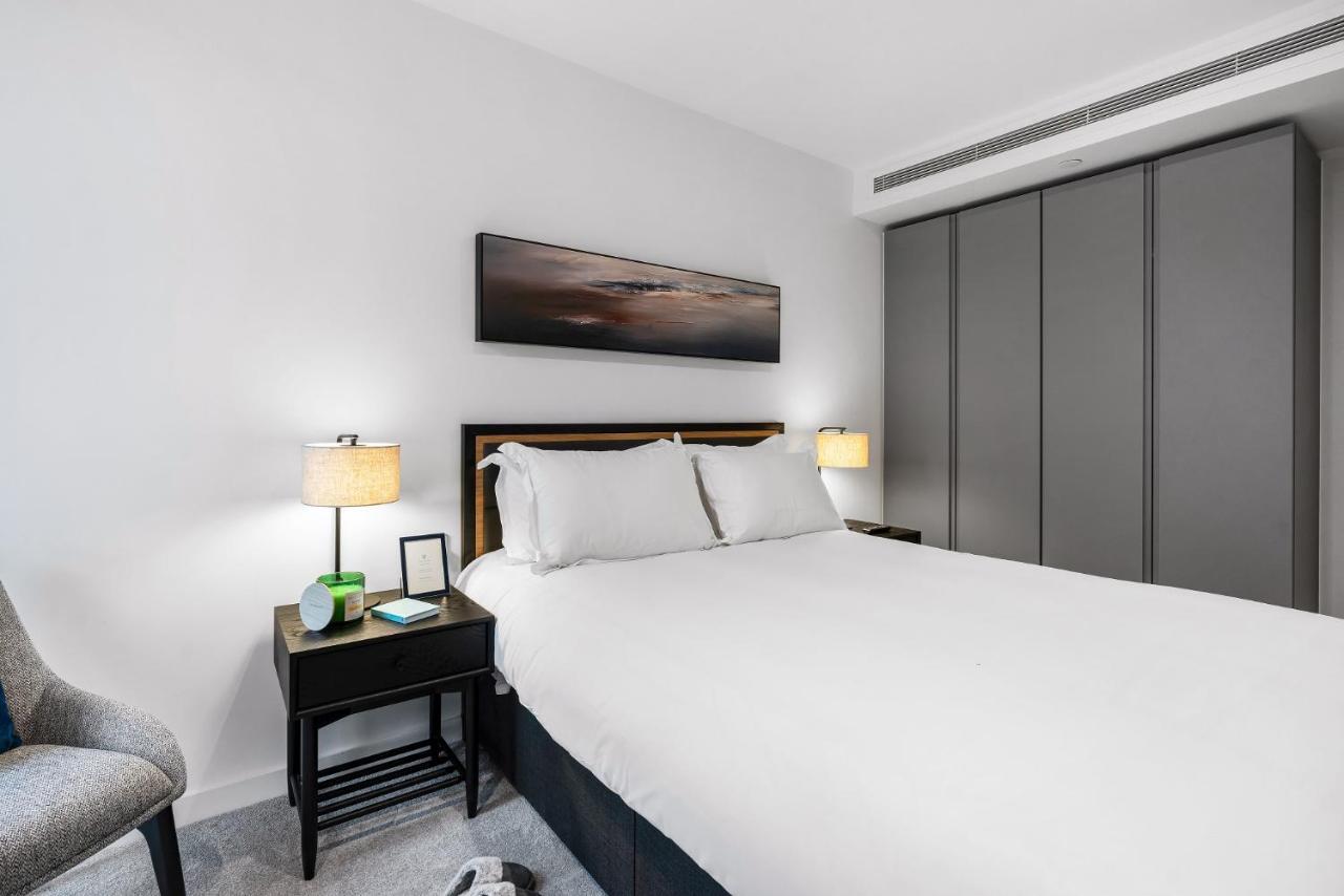 Citysuites 2 Aparthotel Manchester Exterior photo The photo shows a modern bedroom with a neatly made bed featuring white linens and pillows. Flanking the bed are two bedside tables, each with a lamp providing soft lighting. There is a piece of artwork above the bed, which appears to depict a landsc