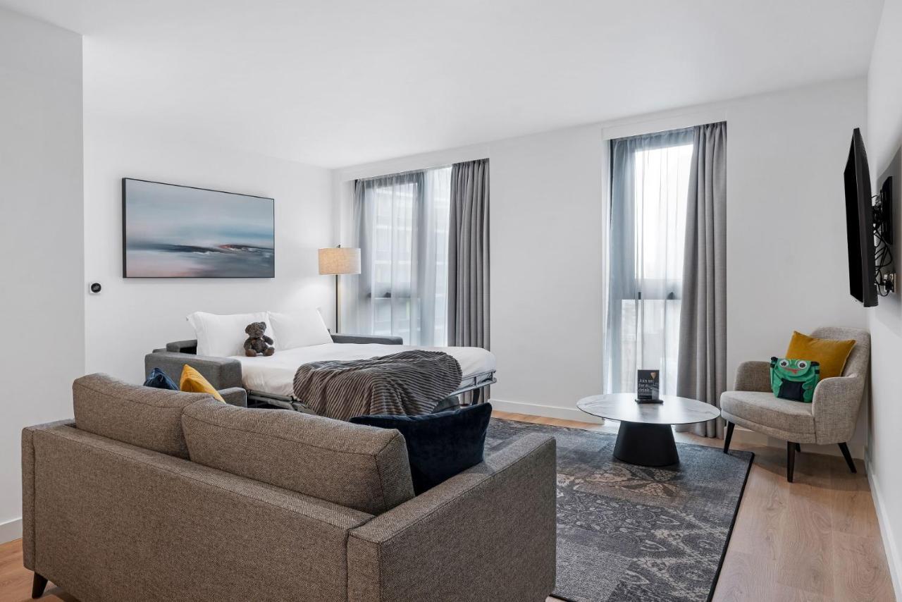 Citysuites 2 Aparthotel Manchester Exterior photo The photo shows a modern living space that incorporates a cozy and inviting atmosphere. It features a light-colored couch with colorful cushions, positioned in front of a coffee table. There's a comfortable armchair nearby, and a throw blanket is dra