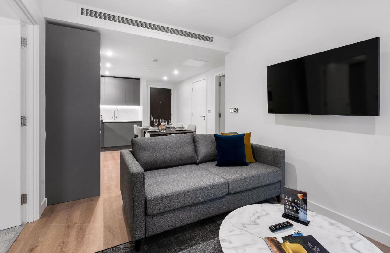 Citysuites 2 Aparthotel Manchester Exterior photo The photo shows a modern living space that includes a gray sofa with colorful cushions, a round marble coffee table, and a flat-screen TV mounted on the wall. In the background, there is a kitchen area featuring sleek cabinets. The flooring is light 