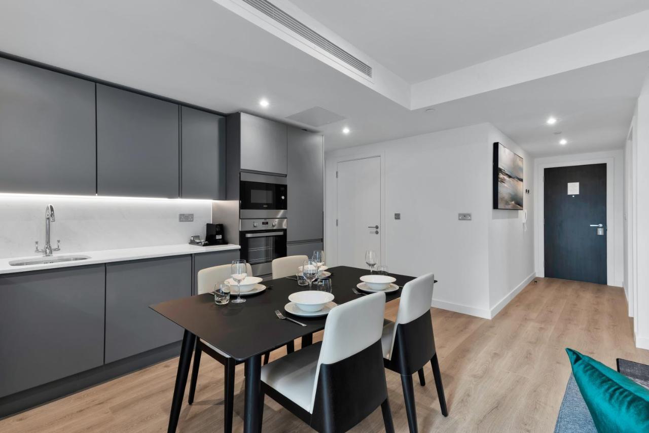 Citysuites 2 Aparthotel Manchester Exterior photo The image shows a modern kitchen and dining area. The kitchen features sleek gray cabinets with a white countertop, and it is equipped with appliances such as a microwave. There’s a dining table set for four, with white plates and glasses ready. The 