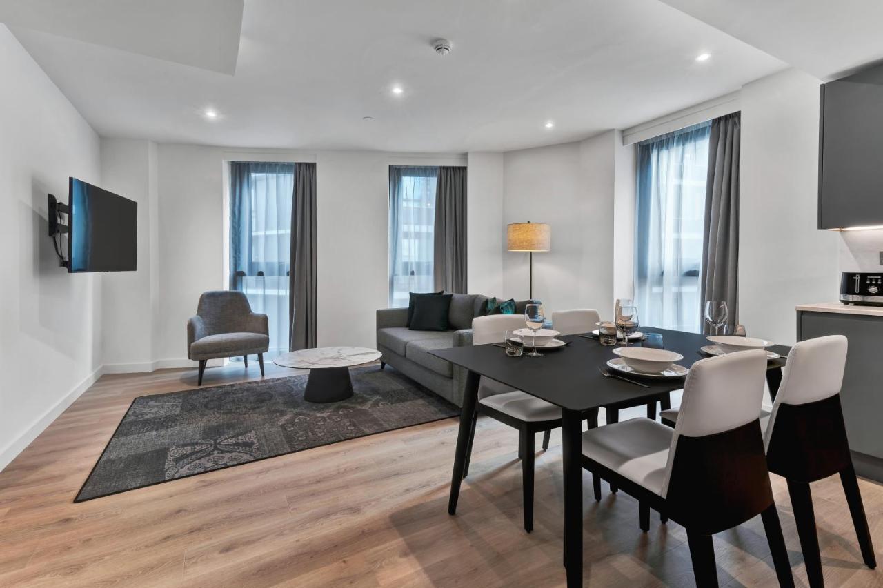 Citysuites 2 Aparthotel Manchester Exterior photo The photo shows a modern living space that includes a living area and dining area. 

- **Living Area**: There's a gray sofa with a coffee table in front of it, along with a single armchair. A large flat-screen TV is mounted on the wall. The space is 