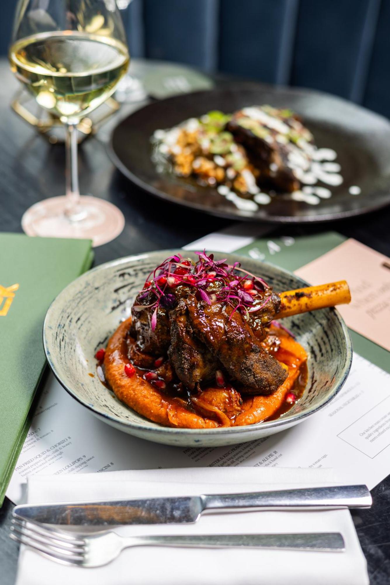 Citysuites 2 Aparthotel Manchester Exterior photo The photo showcases a beautifully presented dish featuring a piece of slow-cooked meat with a bone, likely lamb, sitting atop a vibrant orange puree. The meat is glazed with a rich sauce and garnished with small pieces of red pomegranate and purple m