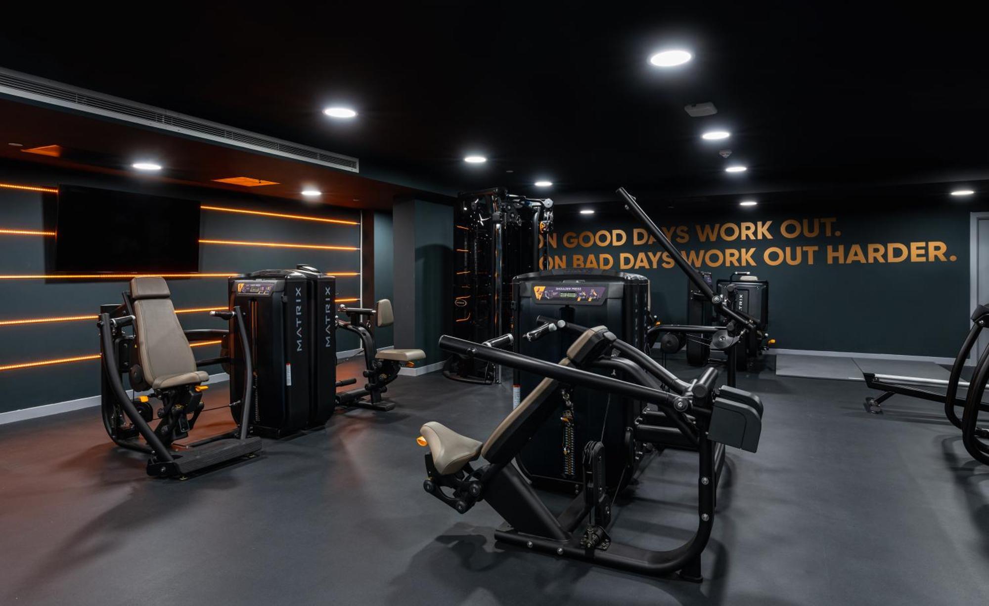 Citysuites 2 Aparthotel Manchester Exterior photo The photo shows a modern gym interior. The gym features various exercise machines, including weight training equipment. The flooring is dark, and the walls are adorned with motivational text that reads, "ON GOOD DAYS WORK OUT. ON BAD DAYS WORK OUT HA