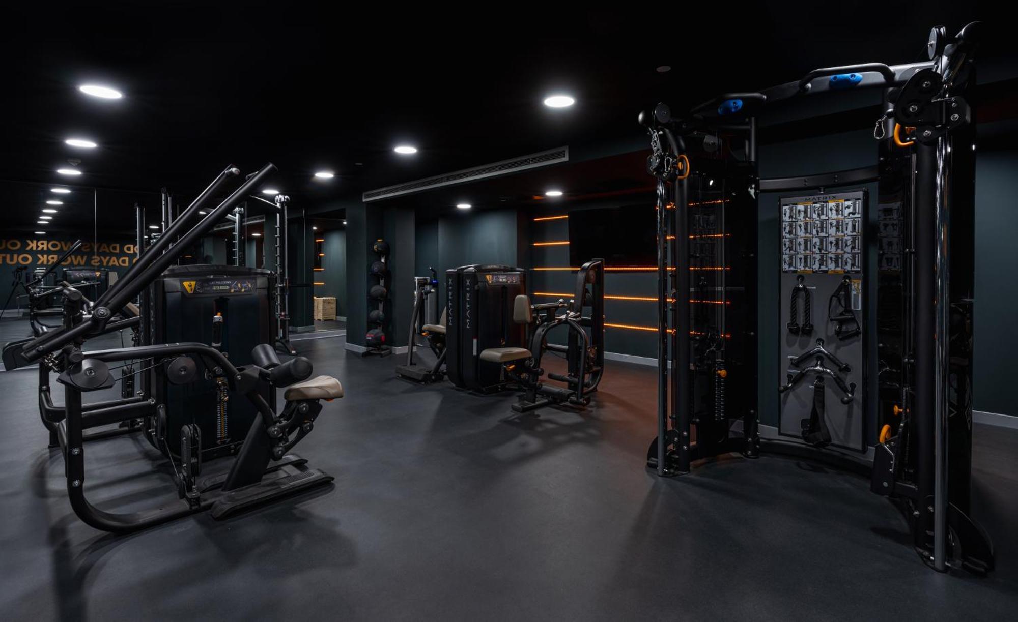 Citysuites 2 Aparthotel Manchester Exterior photo The photo shows a modern gym or fitness area with various workout machines. The space has a dark color scheme, featuring black walls and flooring. There are multiple pieces of exercise equipment, including stations for strength training, possibly tar