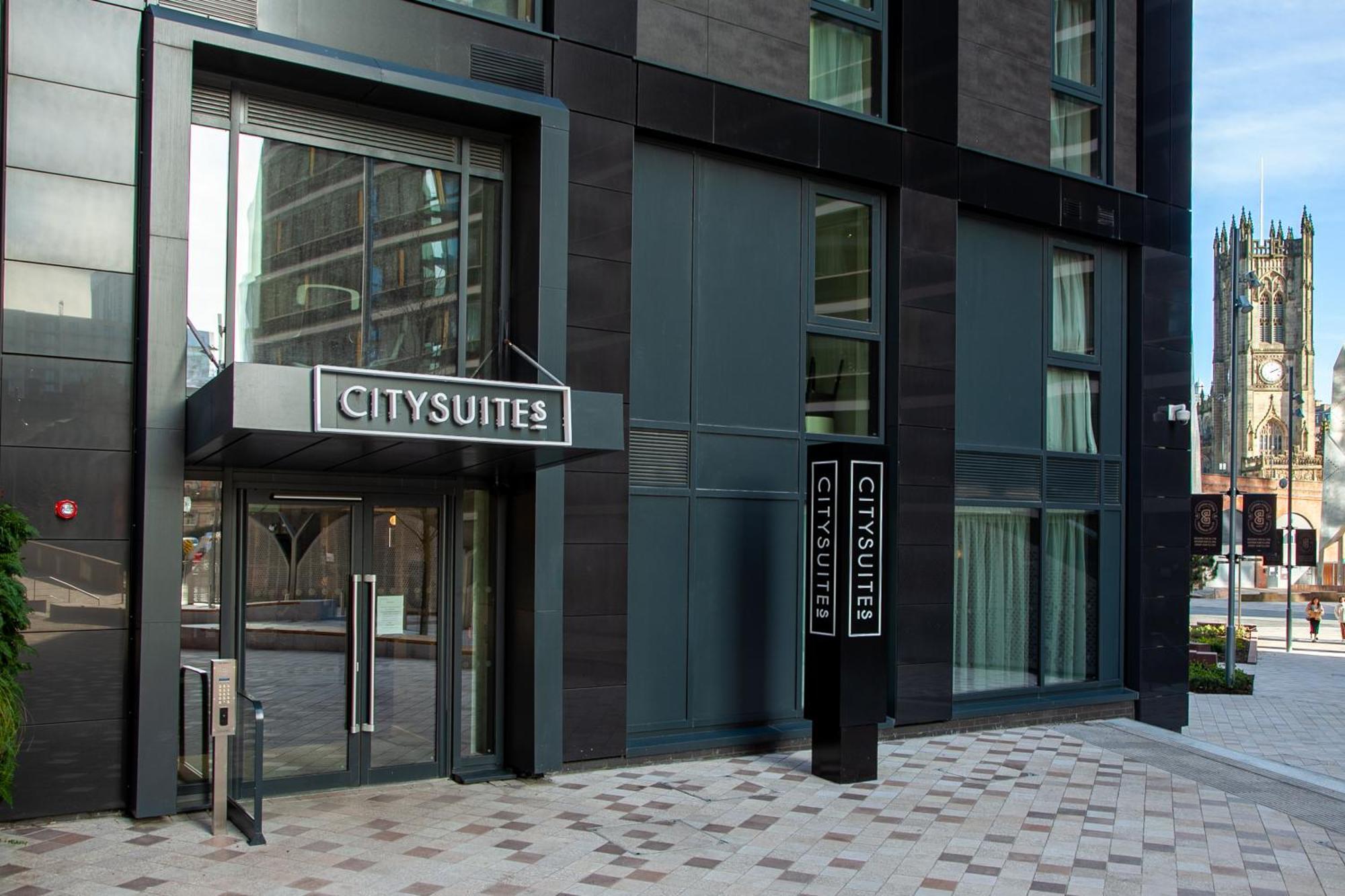 Citysuites 2 Aparthotel Manchester Exterior photo The photo shows the entrance to a modern building labeled "CITYSUITES." The entrance features large glass doors and a sleek, contemporary design. The building has dark exterior panels and large windows, suggesting a stylish and urban environment. The