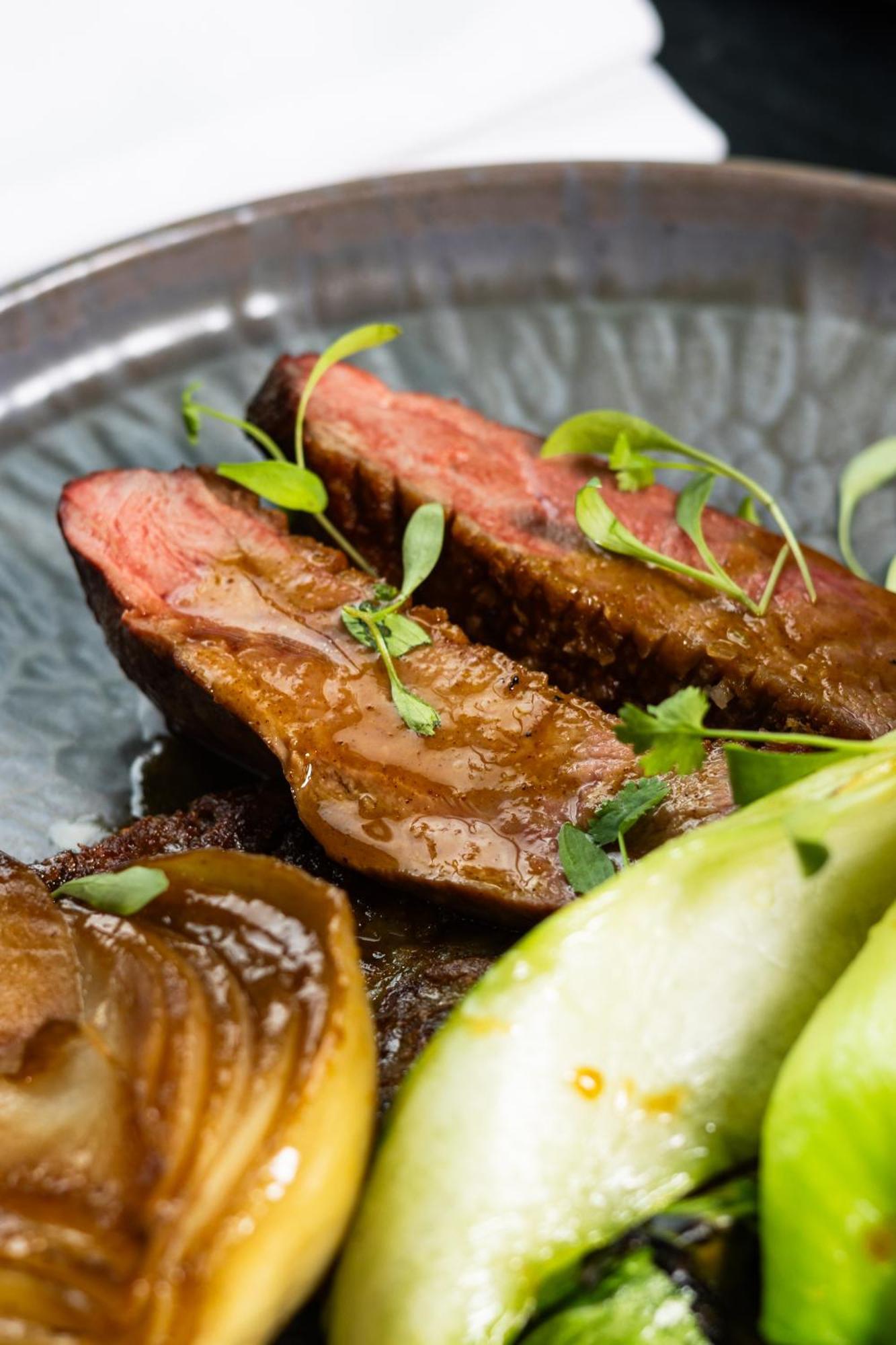 Citysuites 2 Aparthotel Manchester Exterior photo The photo features slices of meat, likely beef, presented on a decorative plate. The meat appears to have a rich brown sauce drizzled over it and is garnished with fresh herbs, adding a pop of green. There are also some slices of a light-colored vege